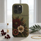 Personalized sage green embroidery effect floral iPhone case from TrioAuraDesign, displayed upright in a bright neutral setting. The smooth printed case features deep burgundy, ivory and dusty rose flowers with botanical greenery, berries and gold-toned details, plus the custom name “Charlotte” near the upper right. Elegant personalized floral phone case with a realistic embroidered look and smooth finish, available in my shop.