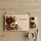 Matching personalized embroidery effect floral MacBook and iPhone cases from TrioAuraDesign, shown together in a top-down lifestyle setting. Both feature deep burgundy, ivory and dusty rose flowers with botanical greenery, berries and gold-toned details on a warm ivory background, plus custom name “Charlotte.” Coordinating smooth printed hard shell covers create an elegant personalized tech set for MacBook and iPhone.