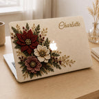 Personalized Crochet effect floral MacBook case from TrioAuraDesign, shown in a warm neutral workspace with an ivory background, deep burgundy, cream and dusty rose flowers, green botanical foliage, berries and gold-toned details. Custom name “Charlotte” appears in elegant gold script, with the Apple logo visible at center. Smooth printed hard shell case with a luxurious floral look for MacBook Air, Pro and Neo models.