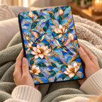 Hands holding Kindle Paperwhite in printed stained glass effect hummingbird case, cozy reading with knit blanket