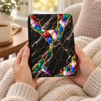 Hands holding Kindle Paperwhite in Jewel Tone black marble case with gold kintsugi seams and colorful opal effect inlays
