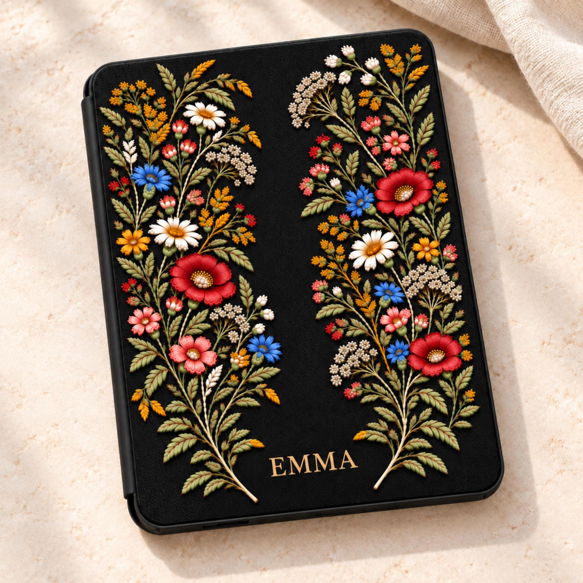 Personalized black Kindle Paperwhite case with embroidery effect wildflowers in burgundy, blue, ivory and gold, with the name EMMA printed in antique gold at the bottom of the front cover