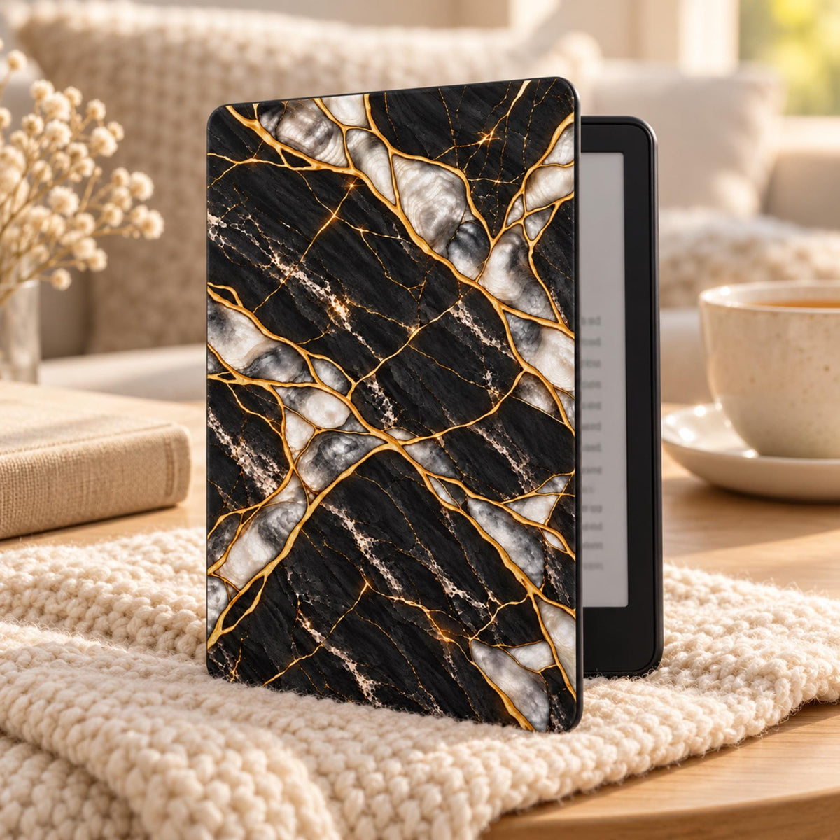 Black Pearl Kindle Paperwhite case with black marble and gold kintsugi effect design standing on a cozy knit blanket next to tea