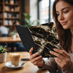 Woman reading in a cafe holding a Kindle in the Black Pearl marble case with gold kintsugi effect seams, showing how the folio case looks in hand